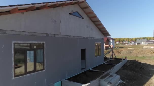 Pohled na fasádu nedokončeného moderního energeticky úsporného domu z pěnových panelů se střechou s kovovými dlaždicemi. Dům ve vesnici. Slunečný den