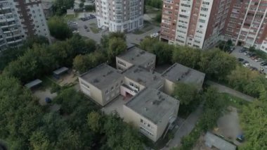 Konut alanındaki boş anaokulu binasının havadan görünüşü. Ağaçlar arasında oyun alanları ve asfaltta çocukların çizimleri var. Şehirdeki anaokulu çok katlı binalar..