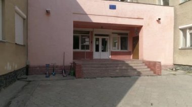 Ağaçları ve oyun alanı olan boş bir anaokulu binası. Ağaçların dalları girişe giden kaldırımın üzerinde asılı.