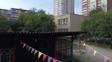 Ağaçları ve oyun alanı olan boş bir anaokulu binası. Ağaçların dalları girişe giden kaldırımın üzerinde asılı.