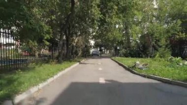 Anaokulu yakınlarındaki asfalt yolu ve ağaçlar arasında inşa edilen drone manzarası. Anaokulunun çevresinde metal çubuklardan yapılmış bir çit var. Yaz günü