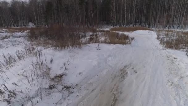 冬のモトクロス雪上トラックにレーサーバイクに乗るの空中ビュー モータトラックの近くに送電線と森林があります 車が道路を走っている — ストック動画