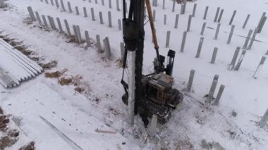 Yığın delici makinenin hava aracı görüntüsü ve kış inşaatında çalışan işçi. Birçok güçlendirilmiş beton yığını zaten makinenin yanındaki yere sürüldü. Bölgede pekçok güçlendirilmiş beton yığını var. Kış bulutlu gün