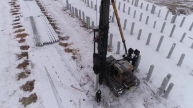 Kış inşaat alanında çalışan bir kazık delici makinenin insansız hava aracı görüntüsü. Birçok güçlendirilmiş beton yığını zaten makinenin yanındaki yere sürüldü. Bölgede pekçok güçlendirilmiş beton yığını var. Kış bulutlu gün