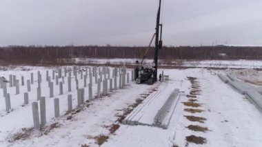 Yığın delici makinenin hava aracı görüntüsü güçlendirilmiş beton yığını kabloyla kaldırmaya hazırlanıyor. İşçi yığından karı temizler. Kış bulutlu gün