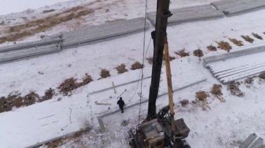 Yığın delici makinenin hava aracı görüntüsü güçlendirilmiş beton yığını kabloyla kaldırıyor. İşçi kabloyu yığına bağlıyor. Kış bulutlu gün