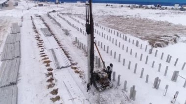 Yığın delici makinenin hava aracı görüntüsü ve kış inşaatında çalışan işçi. Birçok güçlendirilmiş beton yığını zaten makinenin yanındaki yere sürüldü. Bölgede pekçok güçlendirilmiş beton yığını var. Kış bulutlu gün