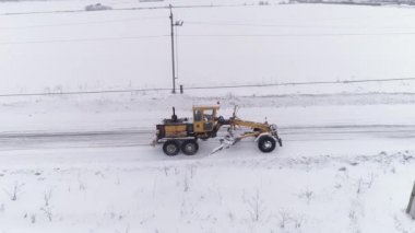 Kar Fırtınası Grader 'ın hava görüntüsü tarla ormanlarının arasındaki Karlı Yol' u temizliyor. Grader köye gidiyor. Yolun kenarlarında elektrik direkleri ve kablolar var. Sert kış koşulları. 