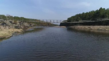 Nehir üzerindeki eski asma köprünün hava aracı görüntüsü. Nehrin kıyısında bir çam ormanı var. Martılar uçuyor. Yaz güneşli bir gün.
