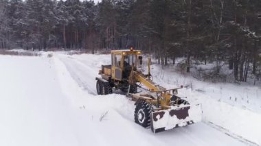 Kar Fırtınası Grader, ormanın yanındaki tarlada Karlı Yol 'u temizledi. Ormandaki mezarlık. Sert kış koşulları. 