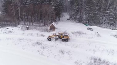 Kar Fırtınası Grader, ormanın yanındaki tarlada Karlı Yol 'u temizledi. Ormandaki mezarlık. Sert kış koşulları. 