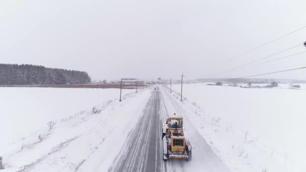 雪送りグレーダーの空中ビューは フィールドを介して冬の雪道を運転しています 道路の両側に電柱やワイヤ 車が運転している 冬曇りの日 — ストック動画