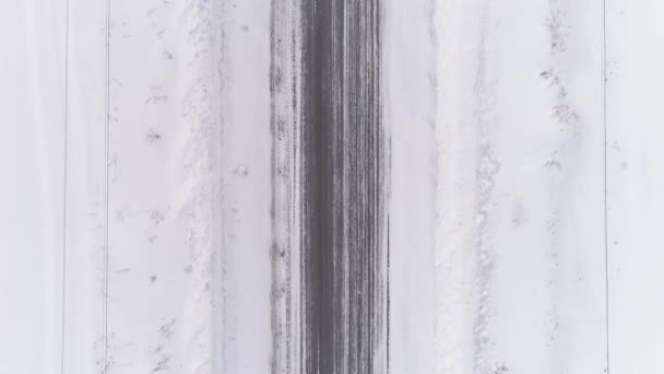 冬の雪道の空中ビューのトップダウン 周りには雪がたくさんあります 道路の両側には ワイヤーで雪のドリフトや電柱があります 車が運転することもある 冬曇りの日 — ストック動画