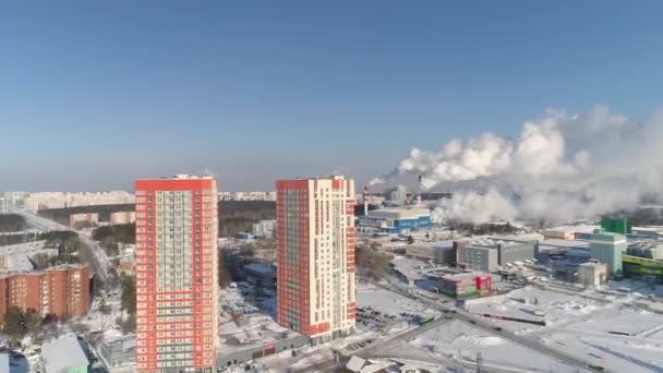 空中俯瞰着两座新的现代橙色摩天大楼 房子后面是一个工业区 管子里冒出大量的烟和蒸汽 以新建高层建筑为背景的现代住宅区 冬日阳光明媚 — 图库视频影像