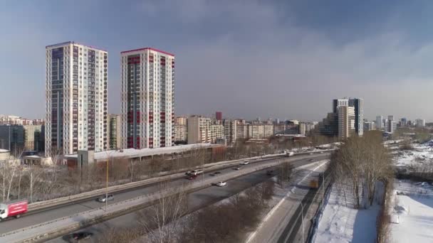 大都市の車のトラフィックと高速道路の空中ビュー 周辺には 遊び場とマルチレベルの駐車場を備えた2つの新しい近代的な高層ビルがあります 近くの典型的なソ連のパネルハウス 街中で雪が降ってる — ストック動画
