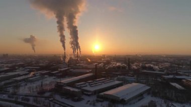 Gün batımında uzun boruları olan büyük bir fabrikanın havadan görüntüsü. Bacalardan duman yükseliyor. Sakin hava, havada duman birikiyor. Kış akşamı, sarı güneş batar. Binaların çatısında kar var..