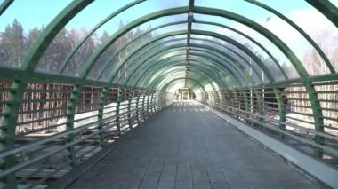 Yeni inşa edilmiş modern yaya köprüsünün içinde yürümek, uzun demir ayak köprüsünün boş olması. Uzun bir koridorda. Köprünün altından arabalar geçiyor.