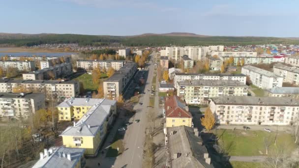 低い建物や池と地方ロシアの都市の空中ビュー 3階建てと5階建ての旧ソ連の家 車が通りを走っている 地平線には山や森が見える 秋の晴れた日 — ストック動画