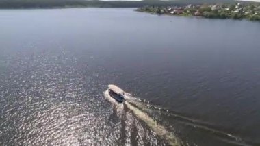 Taşra kentindeki gölette insanlarla dolu küçük bir zevk teknesinin havadan görünüşü. Yakınlarda pek çok tek katlı ve iki katlı ev, köy plajı ve orman var. Yaz güneşli bir gün