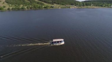 Taşra kentindeki gölette insanlarla dolu küçük bir zevk teknesinin havadan görünüşü. Yakınlarda pek çok tek katlı ve iki katlı ev, köy plajı ve orman var. Yaz güneşli bir gün