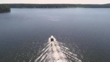 İnsanlarla dolu küçük bir zevk teknesinin havadan görünüşü ormanlı gölette yüzüyor. Yaz güneşli bir gün