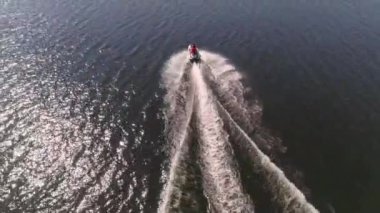 Şehir göletinde jet ski kullanan insanların hava görüntüsü. Jet ski 'deki insanlar uzaklara yelken açıyorlar. Sahilde evler ve ağaçlar var. Diğer kıyıda, orman ve tepelerde. Yaz güneşli bir gün.