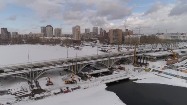 冬季大城市河上公路桥梁重建的空中景观 具有现代的老建筑 在桥梁建筑设备旁边 挖掘机 起重机 — 图库视频影像