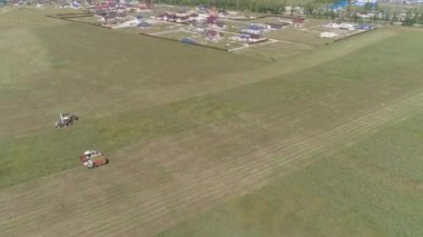 Çim tarlasında hasat yapılan kombine hava görüntüsü. Hasatçılar samanı bir kamyona koyuyorlar. Hasatçılar saman hasadını toplar. Köyün yakınında evler, orman ve sanayi bölgesi var..