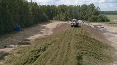 Traktörün insansız hava aracı görüntüsü, orman ve tarlanın yanındaki Silo Çukuru 'ndaki tohumları temizliyor. Hayvanlar için yem. Yaz güneşli bir gün