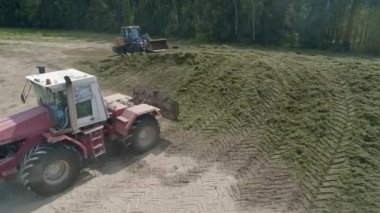 Traktörlerin insansız hava aracı görüntüsü, orman ve tarlanın yanındaki Silo Çukuru 'ndaki filizi tıkıyor. Hayvanlar için yem. Yaz güneşli bir gün