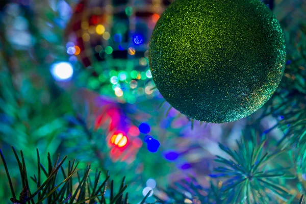 Adorno de Navidad brillante verde colgando de un árbol iluminado —  Fotos de Stock