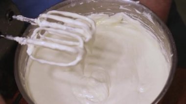 Gümüş kâsenin kenarlarından hamuru kazımak için bir spatula kullanıyor.