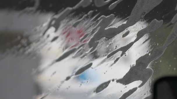 Suds being washed off the outside of a windshield by water drops — Stock Video