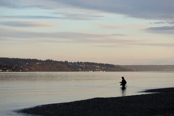 Hombre silueta vadeando en el agua pesca bajo las nubes — Foto de Stock