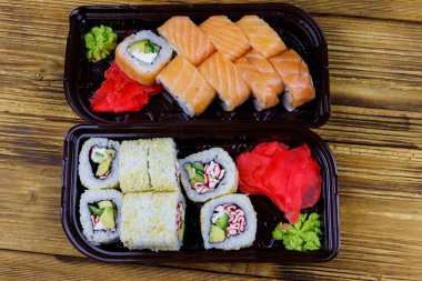 Suşi seti ahşap masada plastik kutularda yuvarlanıyor. Üst Manzara. Plastik kaplarda suşi servis etmek için suşi.