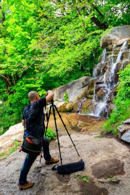 Tripodlu profesyonel kameralı gezgin fotoğrafçı şelalenin fotoğraflarını çekiyor.