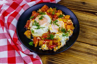 Ev yapımı shakshuka - kızarmış yumurta, soğan, dolmalık biber, domates ve dereotlu ahşap masa. Yahudi mutfağı