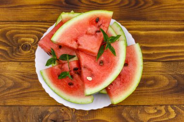 Tahta bir masanın üzerinde beyaz tabakta taze olgun dilimlenmiş karpuz. Üst görünüm