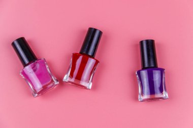 Pastel pembe arka planda tırnak cilası şişeleri. Üst görünüm