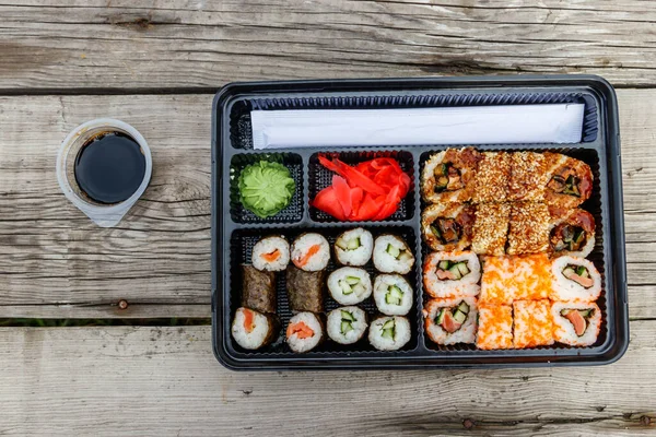 Set of sushi rolls in plastic box on wooden table. Sushi for take away or delivery of sushi in plastic container. Top view