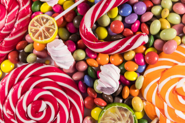 Background of colorful chocolate candies, lollipops, candy cane and marshmallows