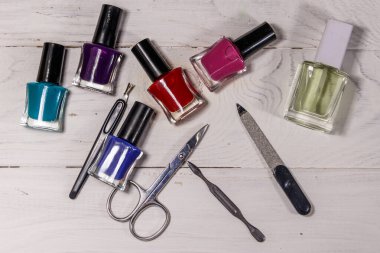 Beyaz ahşap arka planda temel manikür aletleri seti. Tırnak makası, tırnak makası, tırnak törpüsü ve oje şişeleri.