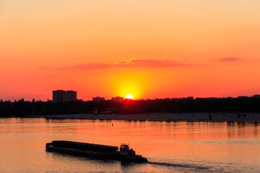 Römorkör, gün batımında Dinyeper nehrinde ağır, uzun bir mavnayı itiyor.