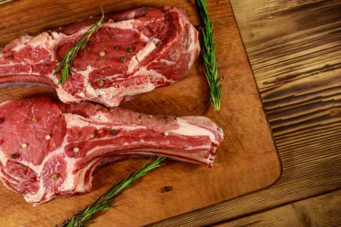 Kemiğin üzerinde çiğ biftek, baharatlar ve ahşap masada biberiye. Üst görünüm