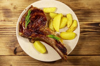 Kemiğin üstünde biftek, fırında patates ve ahşap masada otlar.