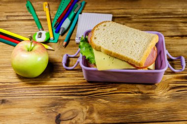 Okul konseptine geri dönelim. Okul gereçleri, elma ve beslenme çantası ve ahşap bir masada sandviçler.