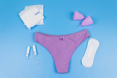 Regl bardakları, hijyenik pedleri ve mavi arka planda tamponları olan kadın külotları. Üst Manzara. Kritik günler, regl dönemi, kadın hijyeni