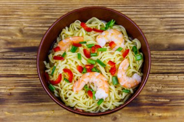 Bir kase karidesli Çin eriştesi, yeşil soğan ve ahşap masada kırmızı acı biber. Üst görünüm