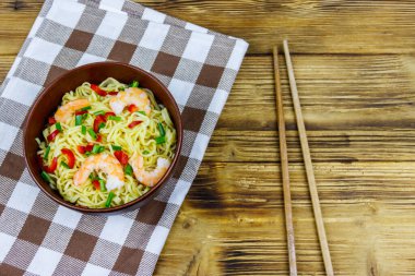 Bir kase karidesli Çin eriştesi, yeşil soğan ve ahşap masada kırmızı acı biber. Üst görünüm