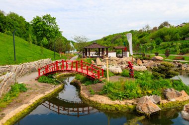 Japon bahçesindeki bir göletin yanında kırmızı köprü ve çardak.